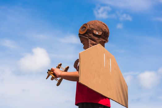 Happy Asian funny child or kid little boy smile wear pilot hat play and goggles with toy cardboard airplane wing flying hold plane toy outdoor against summer blue sky cloud background, Startup freedom