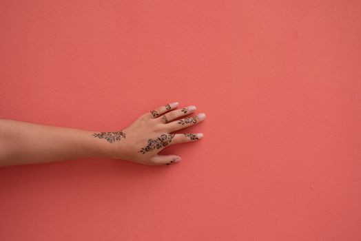 Close up shot of henna covered hand touching pastel colored wall