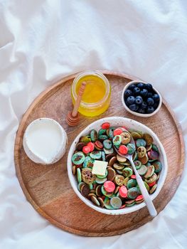 Trendy food - pancake cereal. Bowl of colorful mini cereal pancakes on wooden tray over bed. Tiny pancakes with natural color - green matcha, turquose spirulina, blue pea, red fragon fruit