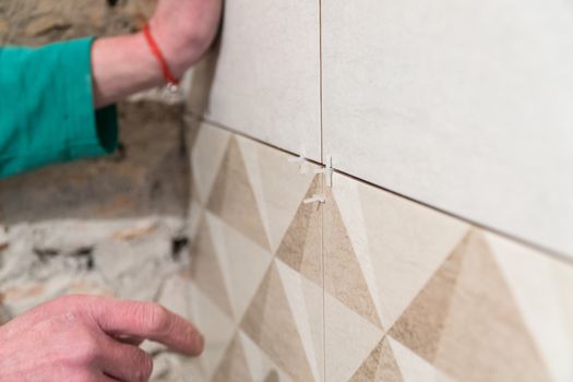 Worker inserts plastic crosses in the seam between tiles. Finishing works, blurred focus. The technology of laying tile.