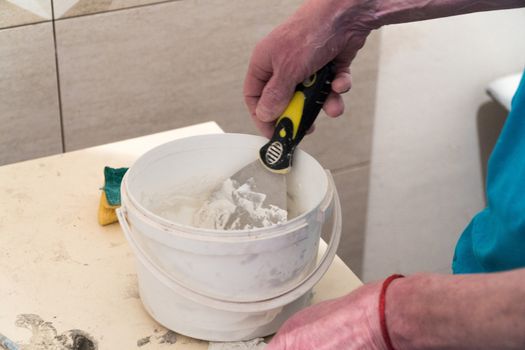 The worker prepares in a bucket putty for tile seams. Finishing works. The technology of laying tile.