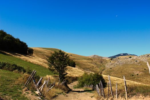 Idyllic view in autumn, on an old mountain road with an old fence and mountain peaks in the background, and clear blue sky. Bjelasnica Mountain, Bosnia and Herzegovina.