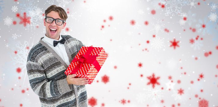 Happy geeky hipster with wool jacket holding present  against snowflake pattern