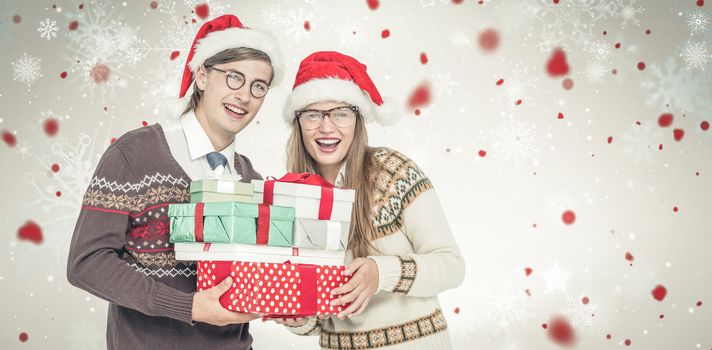 Portrait of smiling man and woman wearing Santa hats and holding gifts  against snowflake pattern