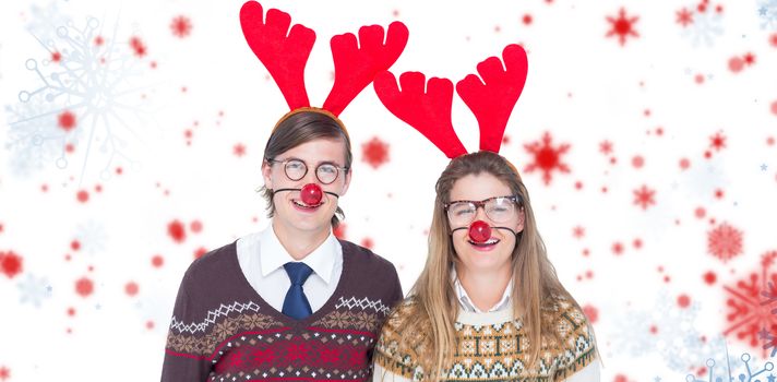 Portrait of smiling man and woman wearing red reindeer horn  against snowflake pattern