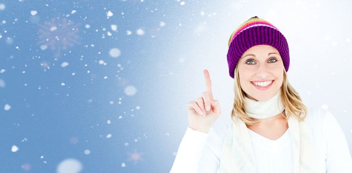 Joyful woman with a colorful hat pointing upwards against snow