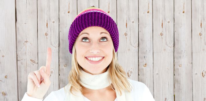 Bright woman with a colorful hat pointing upwards against wooden background