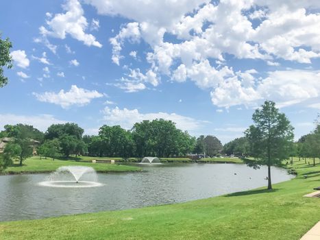 Double floating fountains at residential park in Coppell, Texas, America. Beautiful local park with lush trees and green grass lawn under sunny cloud blue sky.