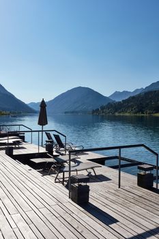 Hotel terrace with deck chairs on the shores of an alpine lake surrounded by mountains