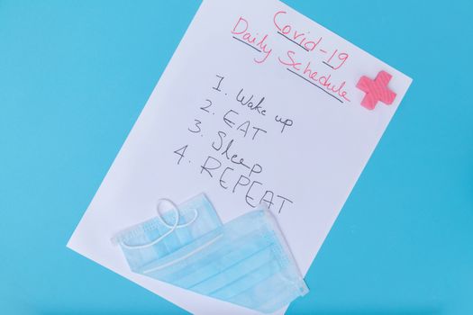 Concept of coronavirus lockdown daily schedule wake up, eat, sleep, repeat quote on paper due to Covid-19 outbreak or pandemic with medical face mask