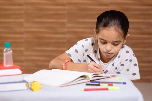 Little schoolgirl busy in doing homework with hand sanitizer in front during coronavirus or covid-19 outbreak - Concept of homeschooling, children education.