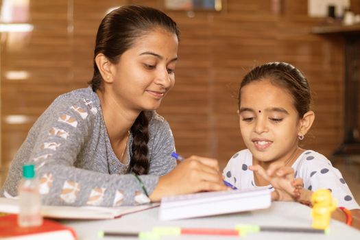 young girl teaching her sister at home - concept of homeschooling during coronavirus or covid-19 lockdown pandemic