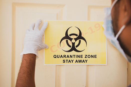 Frontline worker applying banner of Covid-19 or coronavirus quarantine zone stay away infront of the door at hospital as caution note
