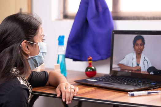 Concept of Online Chat, telehealth, or tele counseling with Nurse or Doctor on Screen during coronavirus or covid-19 pandemic - Girl in medical mask listening to doctor on laptop at home.