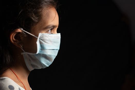 Young teenager girl with medical face mask in dark room at home quarantine due to covid 19 or coronavirus outbreak