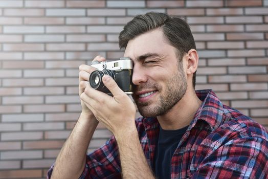 Man with retro photo camera Fashion Travel Lifestyle outdoor while standing against brick wall background.