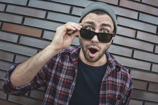 Shocked caucasian man in sunglasses standing at brick background.