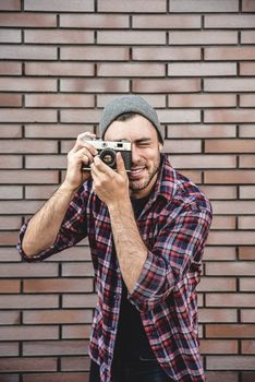 Man with retro photo camera Fashion Travel Lifestyle outdoor while standing against brick wall background.