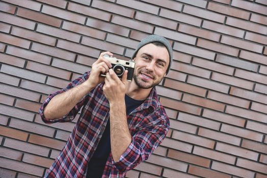 Man with retro photo camera Fashion Travel Lifestyle outdoor while standing against brick wall background.