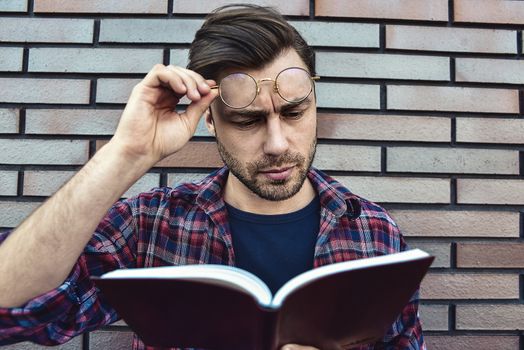 Portrait of smiling handsome man in round glasses and shirt isolated on brown brick wall.