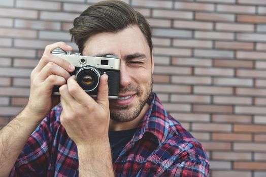 Man with retro photo camera Fashion Travel Lifestyle outdoor while standing against brick wall background.