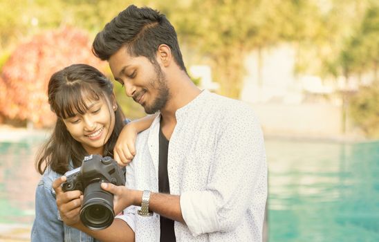 Cute Couple looking pictures on camera screen - Happy Young professional Photographer showing Images to model on his DSLR - concept of model and cameraman working together