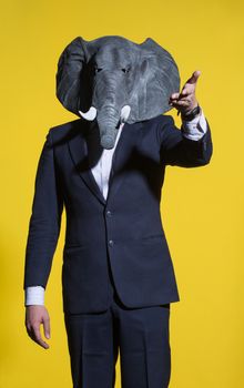 A man in a suit and an elephant mask on a yellow background. Conceptual business background