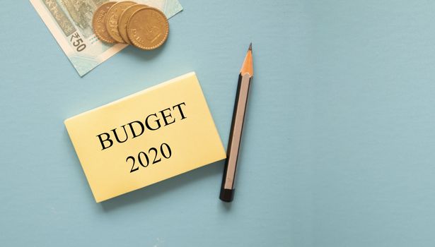 Concept of Budget 2020 with Indian Currency notes and coins on blue background with copy space