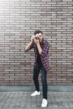 Man with retro photo camera Fashion Travel Lifestyle outdoor while standing against brick wall background.