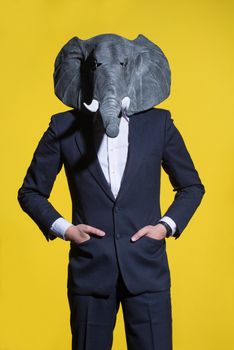 A man in a suit and an elephant mask on a yellow background. Conceptual business background