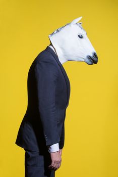 A man in a suit and a horse mask on a yellow background. Conceptual business background