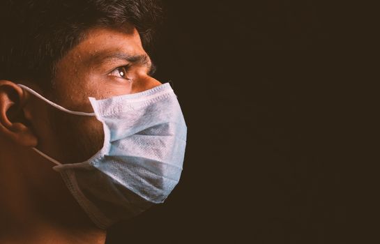 Young man wearing medical face mask to protect from spreading coronavirus outbreak infection in dark room and thinking of virus attack