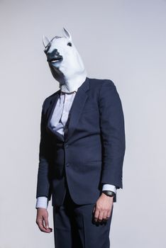 A man in a suit and a horse mask on a light background. Conceptual business background