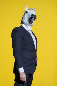 A man in a suit and a horse mask on a yellow background. Conceptual business background