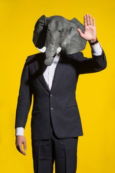 A man in a suit and an elephant mask on a yellow background. Conceptual business background