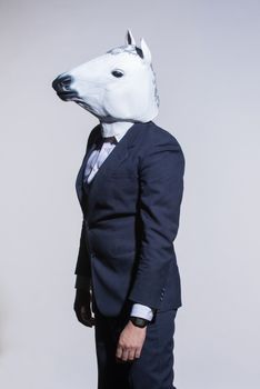 A man in a suit and a horse mask on a light background. Conceptual business background