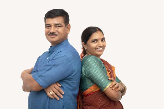 Happy Indian couples in traditional dress with arms crossed standing back to back on isolated background - concept of happy, love and cheerful couple relationship