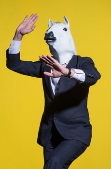 A man in a suit and a horse mask on a yellow background. Conceptual business background