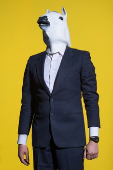 A man in a suit and a horse mask on a yellow background. Conceptual business background