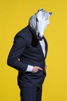 A man in a suit and a horse mask on a yellow background. Conceptual business background