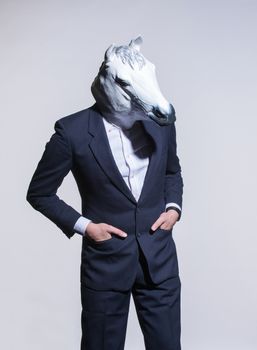 A man in a suit and a horse mask on a light background. Conceptual business background