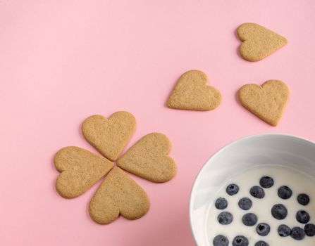 Breakfast. Close-up of heart shaped cookies like flower petals. A bowl of yogurt with blueberries. Pink background. Copy space.