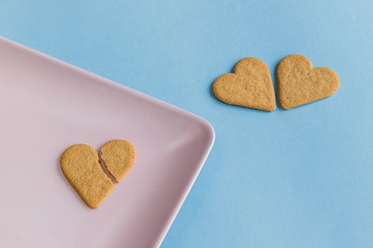 Broken heart. Cookies like a romantic and dramatic scene. Heart shaped cookies. Pink and light blue background. Copy space.