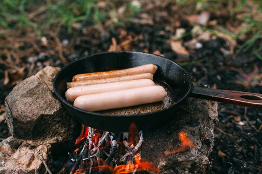 Roasting sausages in a frying pan over an open fire. Preparing food in nature. Lunch in the open air. Picnic in the forest. Food on fire