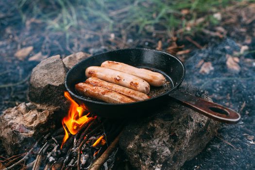 Roasting sausages in a frying pan over an open fire. Preparing food in nature. Lunch in the open air. Picnic in the forest. Food on fire