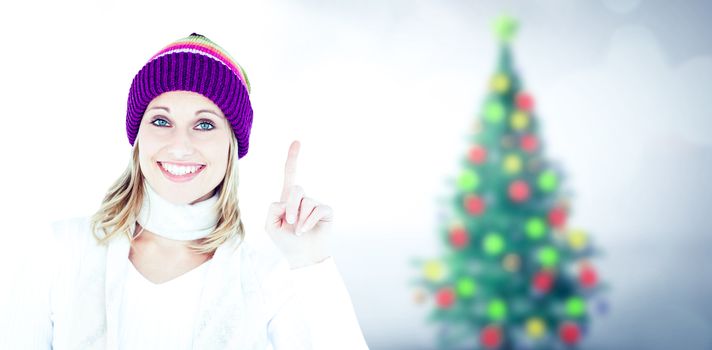 Joyful woman with a colorful hat pointing upwards against blurry christmas tree in room