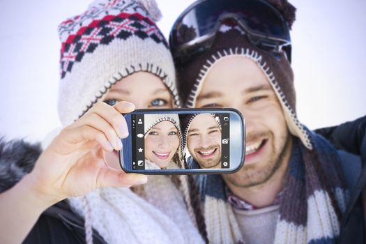 Hand holding smartphone showing against close up portrait of a smiling couple in woolen hats