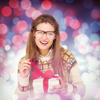 Happy geeky hipster smiling at camera and holding present against snowflake pattern