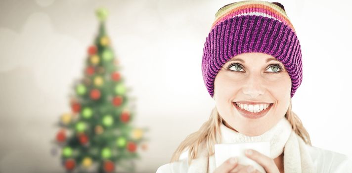 Smiling woman with a colorful hat and a cup in her hands against blurry christmas tree in room