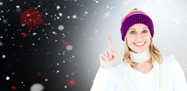 Joyful woman with a colorful hat pointing upwards against snow